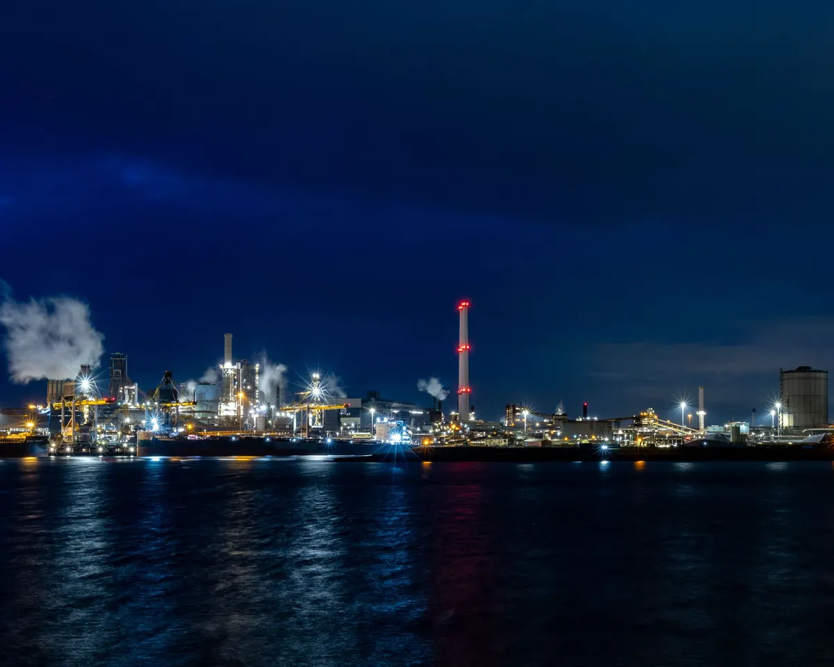 Verlicht industrieterrein in de avond, weerspiegeld in het water