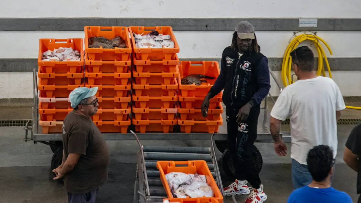 Medewerkers bij gestapelde kratten met vis in een visverwerkend bedrijf