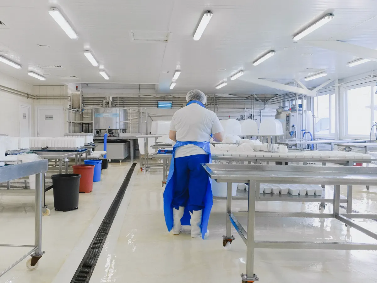 Medewerker in hygiënekleding in een lichte productieruimte met RVS-werktafels