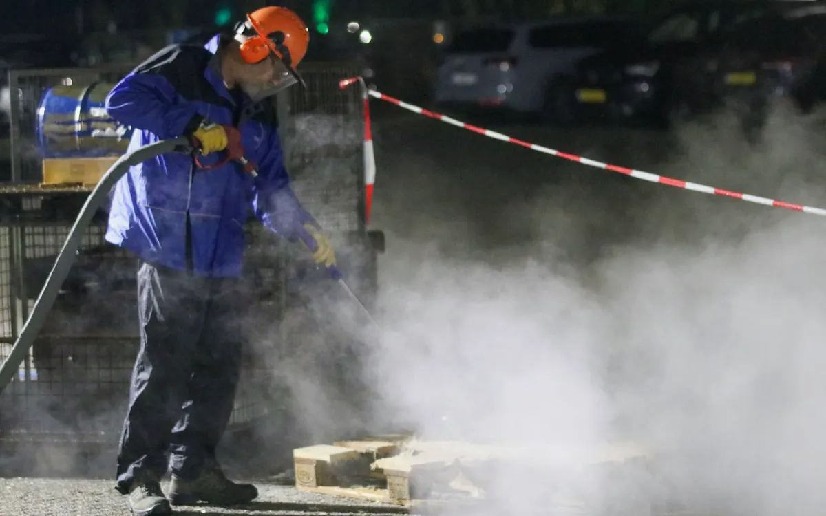 Medewerker in beschermende kleding reinigt met een heetwater-hogedrukreiniger, met stoomwolken