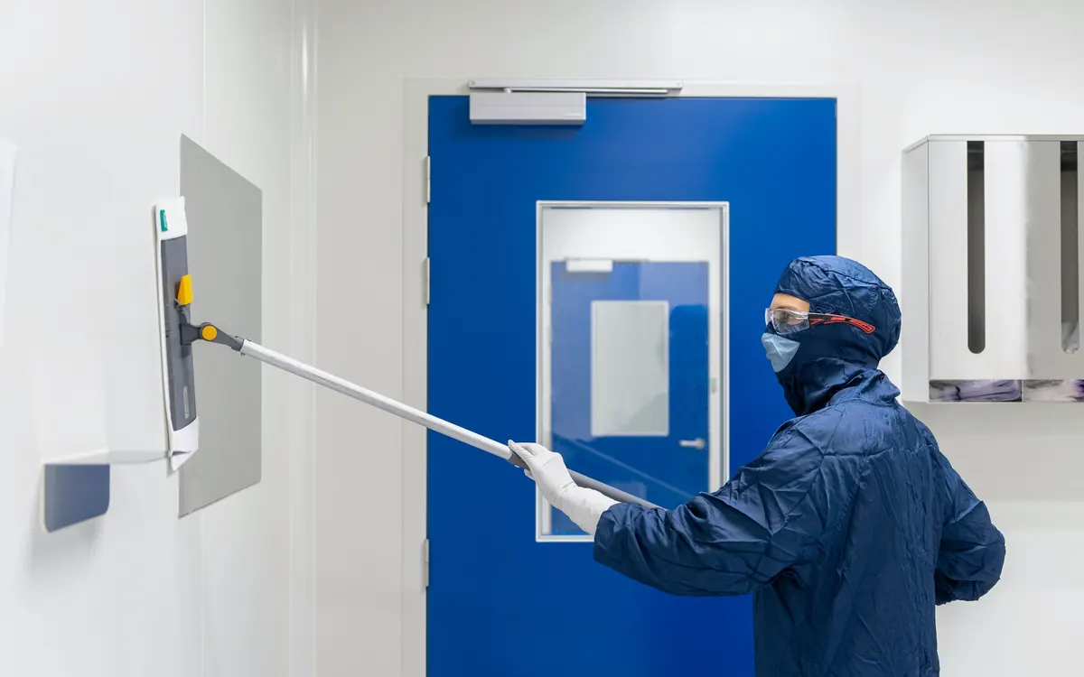 Medewerker in beschermende kleding reinigt een wand in een hygiënische ruimte
